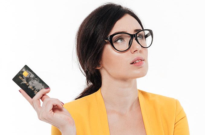 Woman with eyeglasses holding a credit card looking perplexed