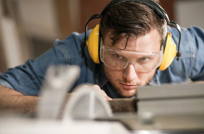 man wearing safety goggles and headphones while working with a saw