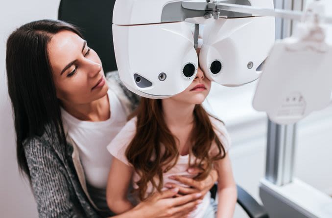 Girl sitting on her mother's lap to perform eye test and define her visual acuity